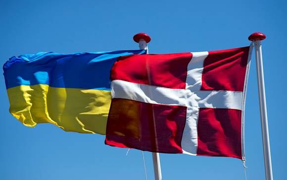 Det ukrainske og det danske flag vajer ved siden af hinanden mod blå himmel.