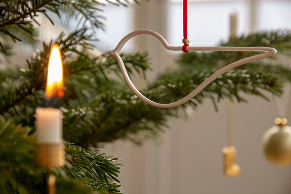 Tændt stearinlys står i sin stage på et juletræ med pynt 