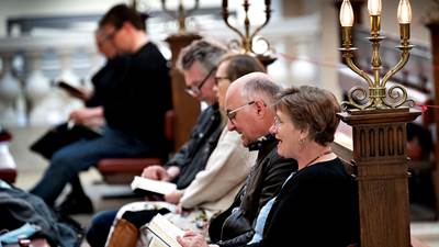 Seks kirkegængere sidder på bænke i Vor Frue Kirke i København og synger under gudstjeneste.