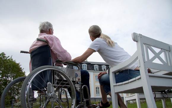 En ældre mand i kørestol på plejehjem og en kvinde