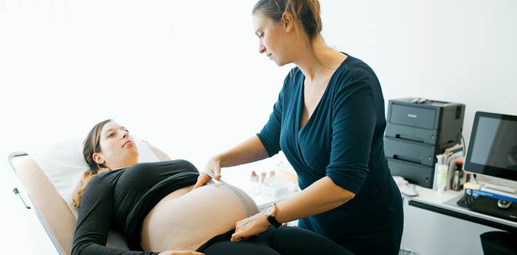 Gravid kvinde får undersøgt sin mave med et målebånd