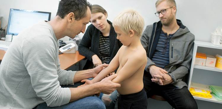 Fem-seks årig dreng undersøges af læge, mens forældre kigger til